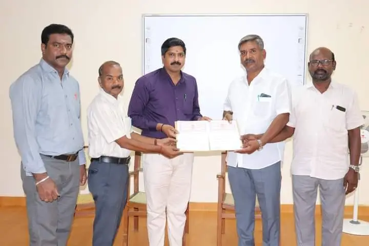 Six men in a classroom; two of them hold up a signed agreement.