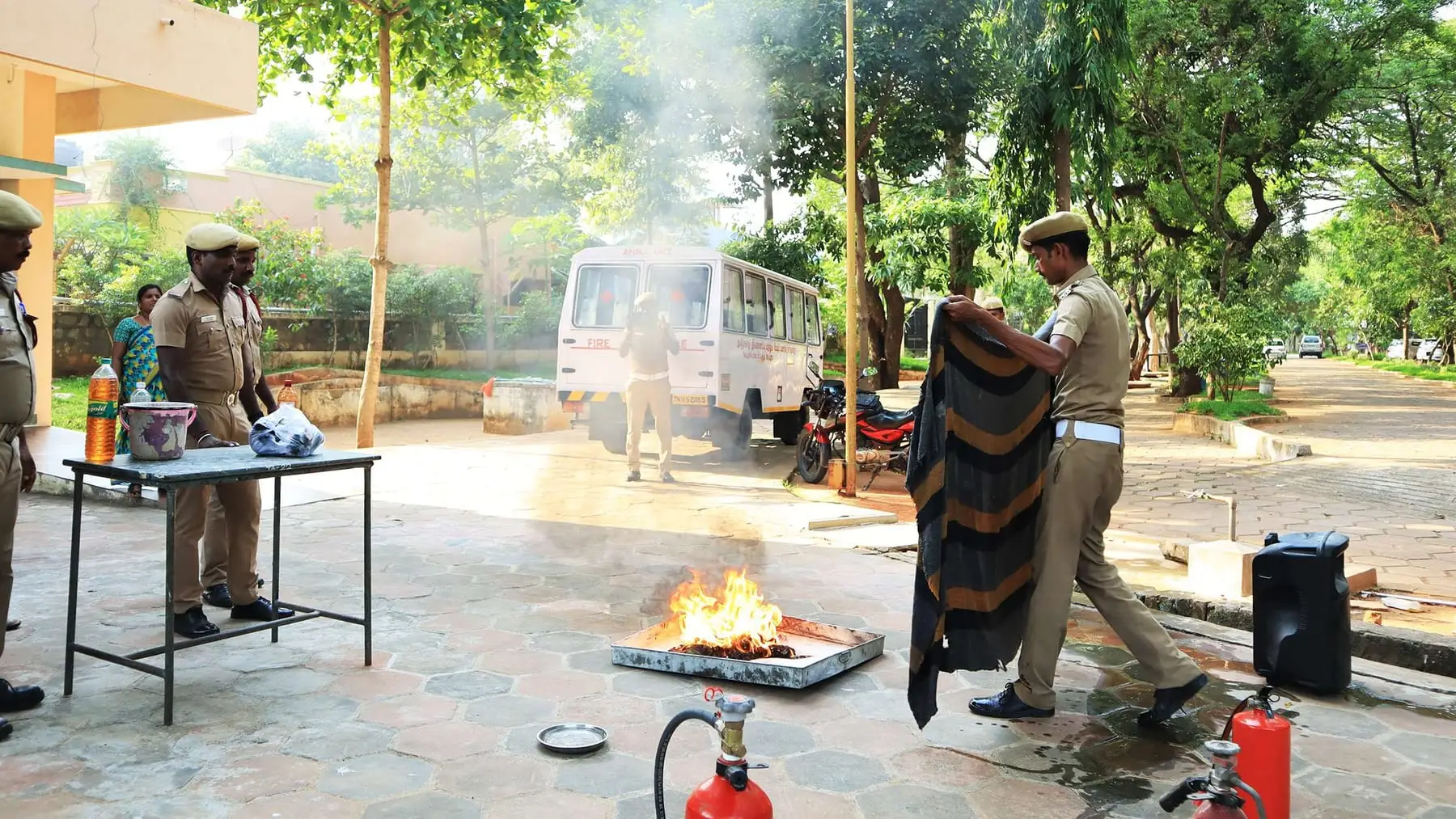 Fire service officers show students how to put out a fire, outdoors.