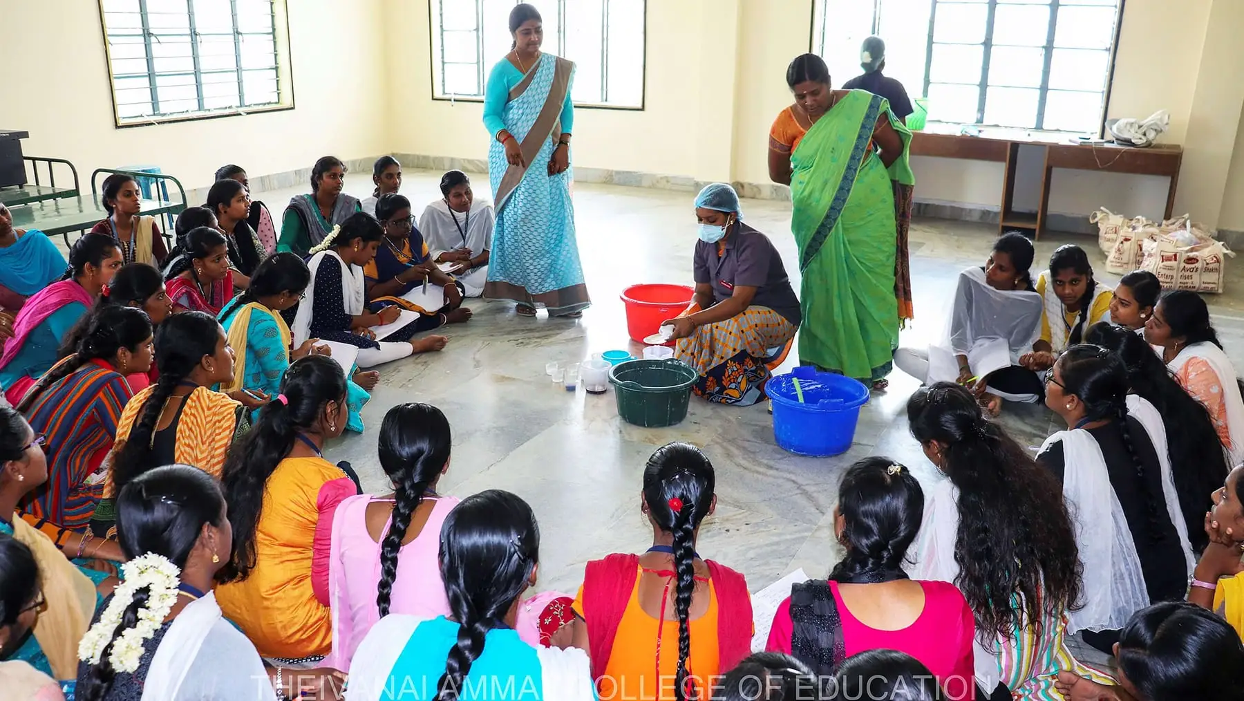 Students sit on the floor around bowls and buckets during a hands-on session.